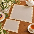 Beżowe serwetki Lena z koronką w dwóch rozmiarach 20x20 i 30x30 – aranżacja na drewnianym stole z porcelanowym imbrykiem, herbatą i kwiatami.