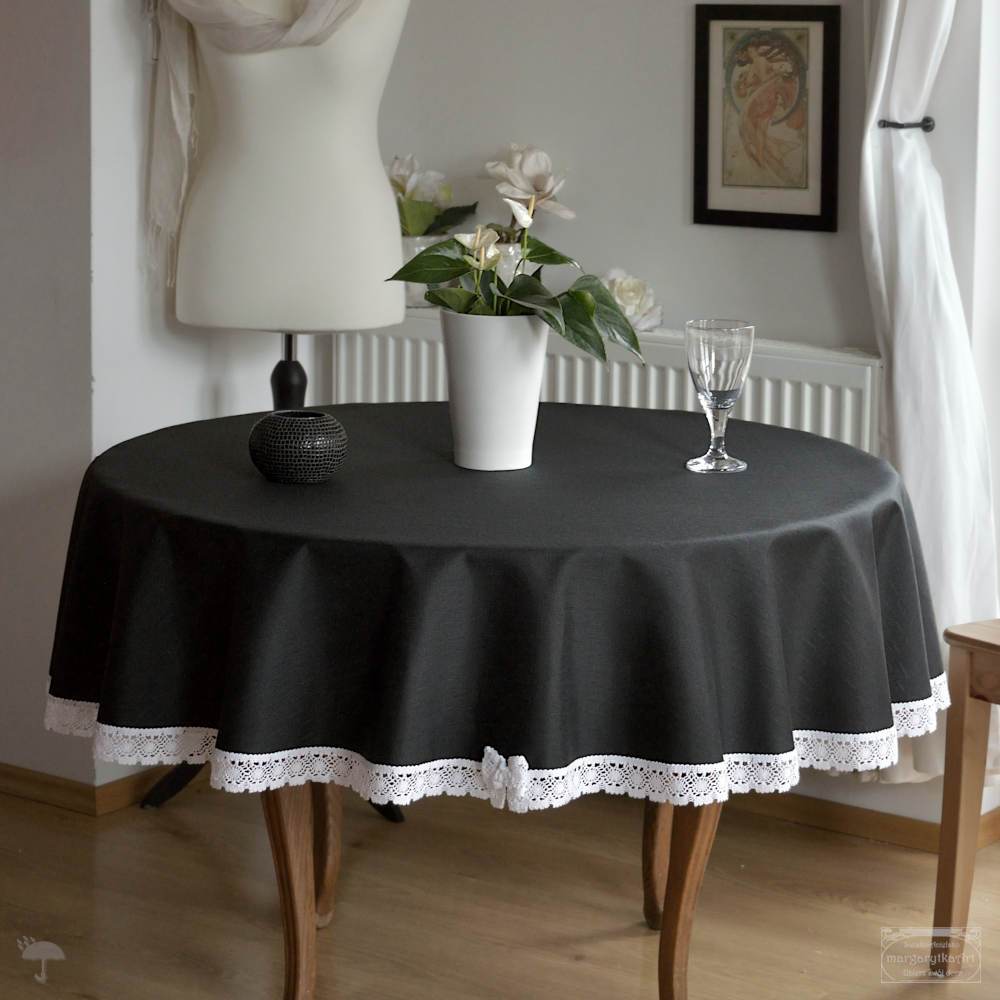 Elegancka aranżacja stołu z okrągłym czarnym obrusem ozdobiony białą koronką i finezyjną kokardką